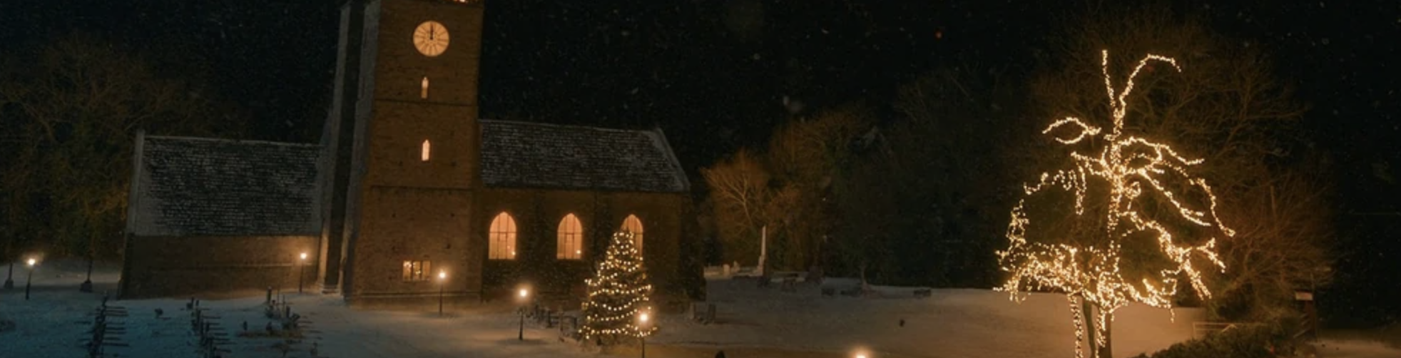 A screencap from "The Church on Ruby Road." It's of the titular church, in the snow, pleasantly lit by Christmas lights.